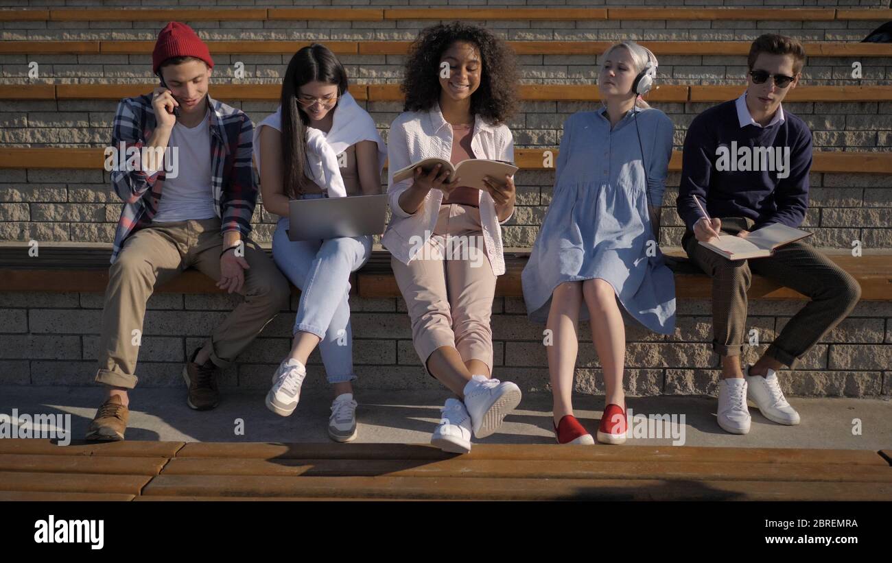 Group of young people sitting together doing different things. Stock Photo