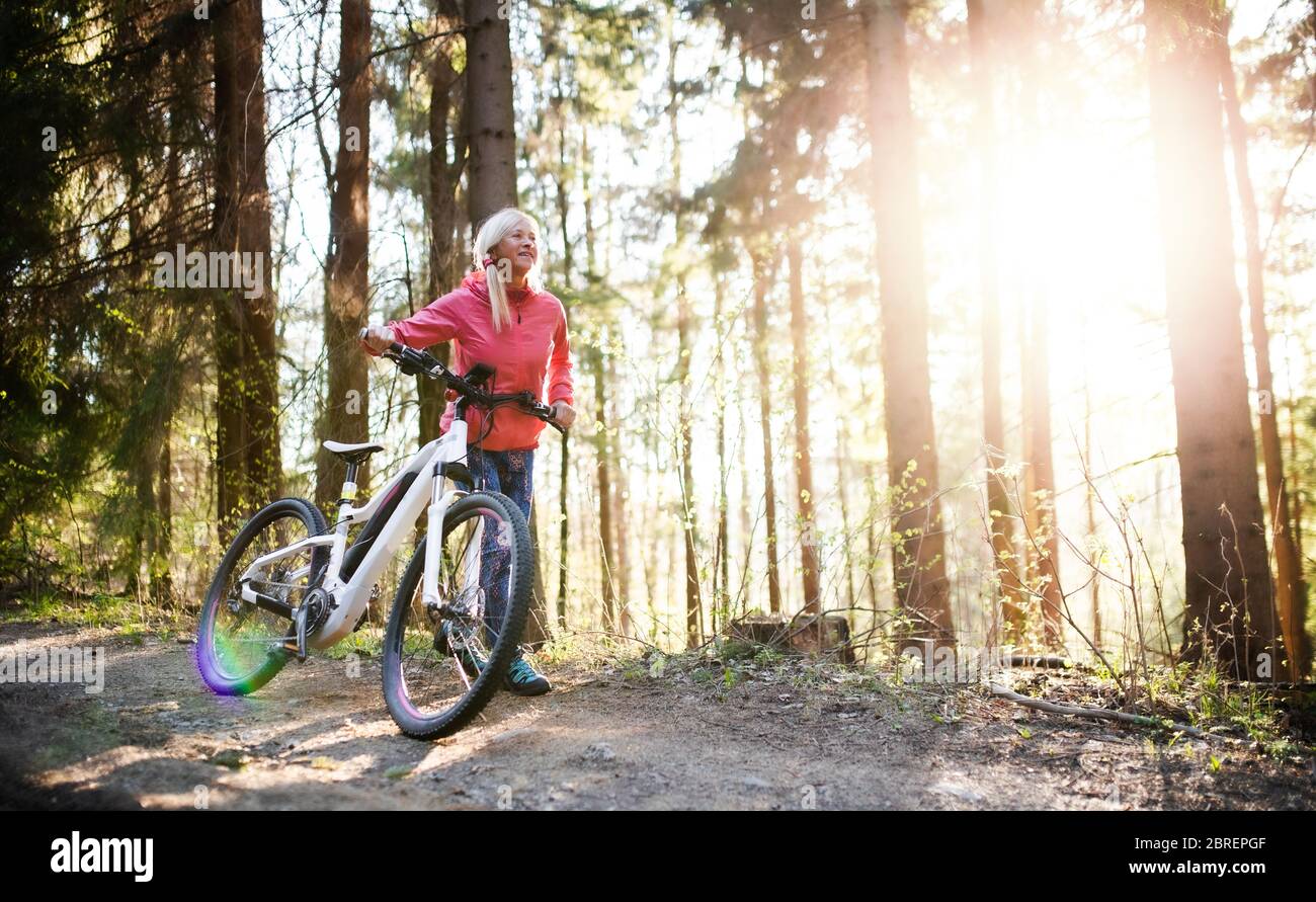 Active senior woman with e-bike cycling outdoors in nature. Stock Photo