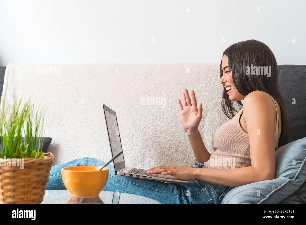 Young woman making video call sitting on sofa - Happy girl having fun doing video conference with family and friends Stock Photo