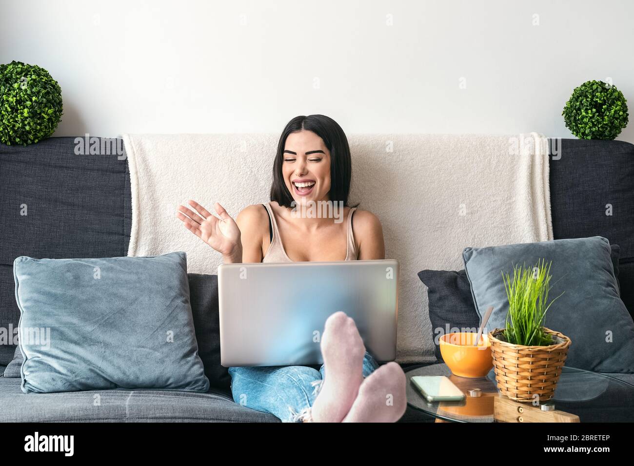 Young woman making video call sitting on sofa - Happy girl having fun doing video conference with family and friends Stock Photo