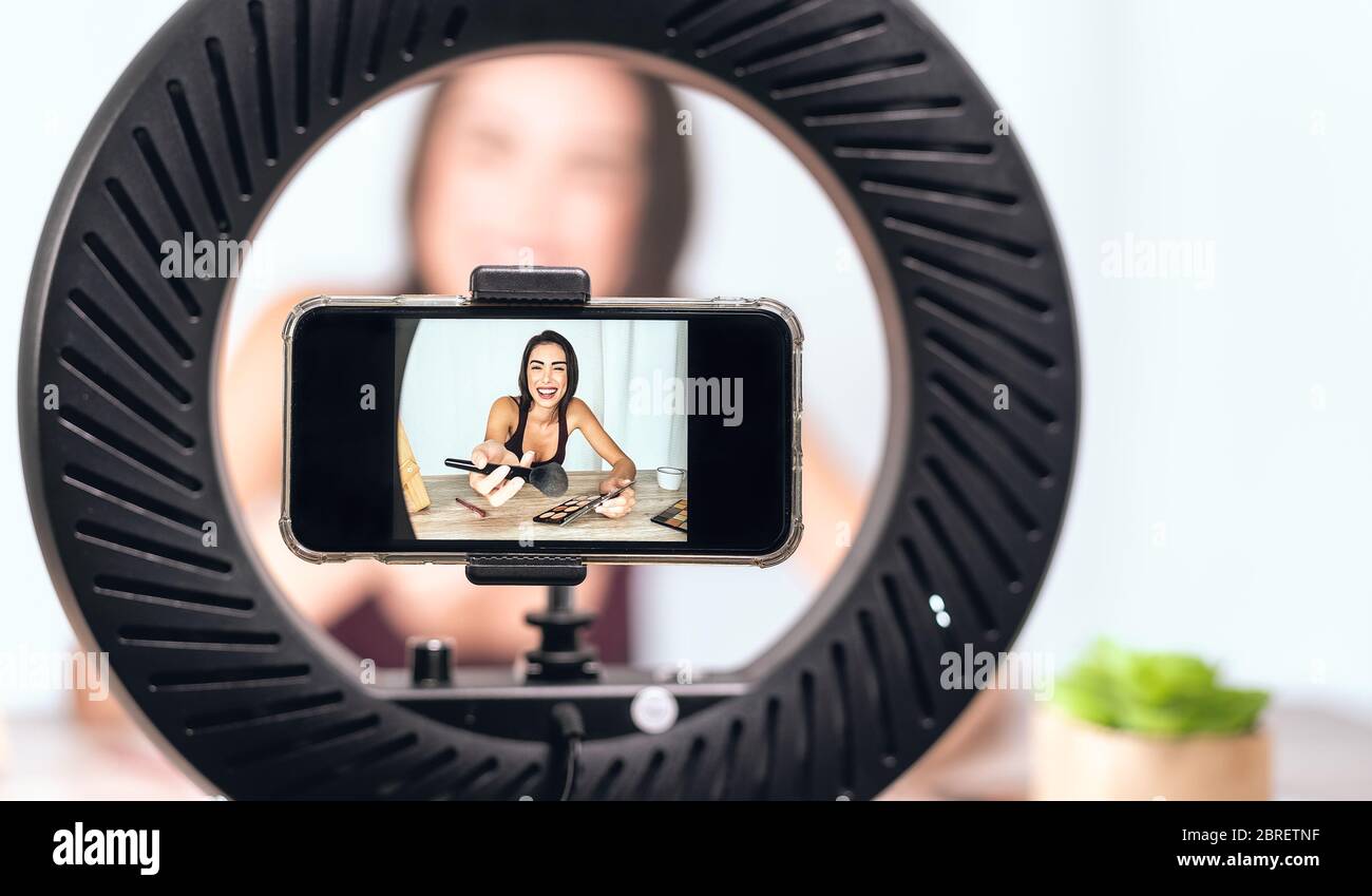 Young female vlogger doing makeup tutorial video for web channel at home - Happy influencer girl having fun filming with mobile smartphone Stock Photo