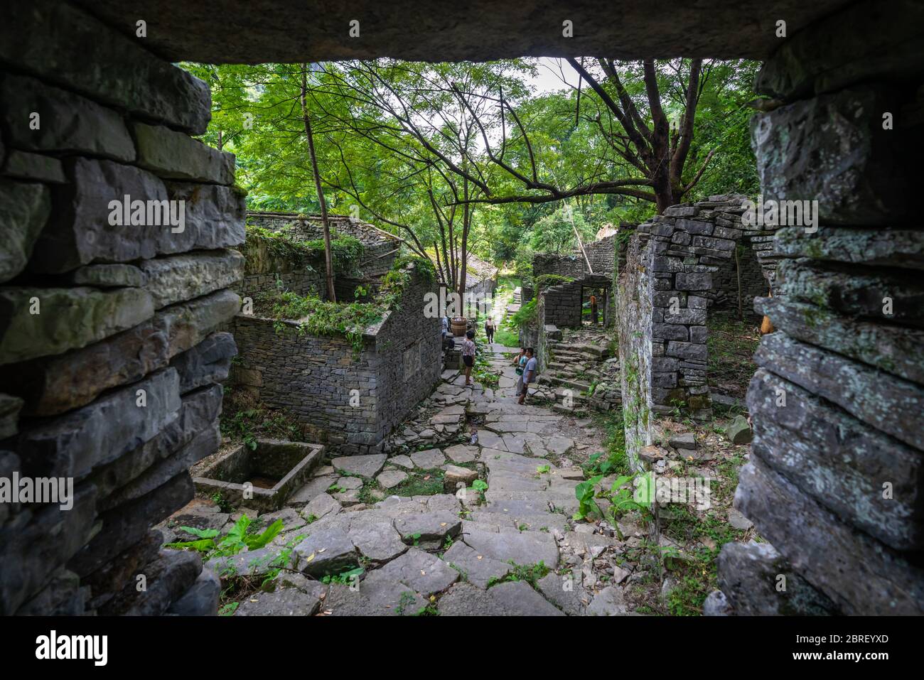 Yangshuo, China - August 2019 : Group of tourists standing on a pathway of concrete steps among old abandoned houses of an old village located in the Stock Photo