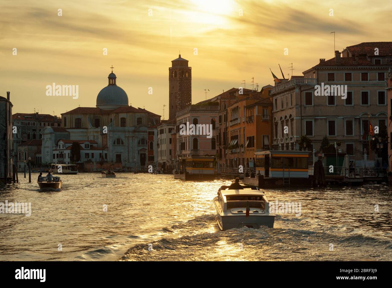 Water taxis are sailing along the Grand Canal at sunset in Venice, Italy. Grand Canal is one of the major water-traffic corridors in Venice. Stock Photo