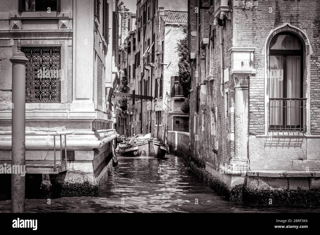 The narrow side street with a boat at Grand Canal in Venice, Italy. Vintage view of Venice canals in black and white. Old buildings and cityscape of V Stock Photo