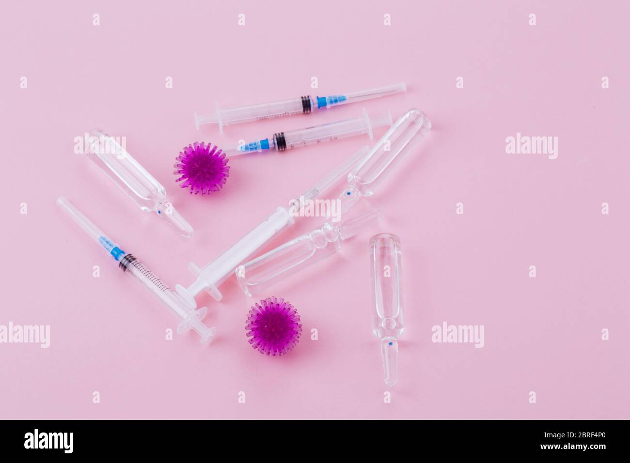 Abstract model of coronavirus infection of the strain Coronavirus.Purple virus, syringe and ampoules with medicine on a pink background, poses a pandemic hazard. Stock Photo