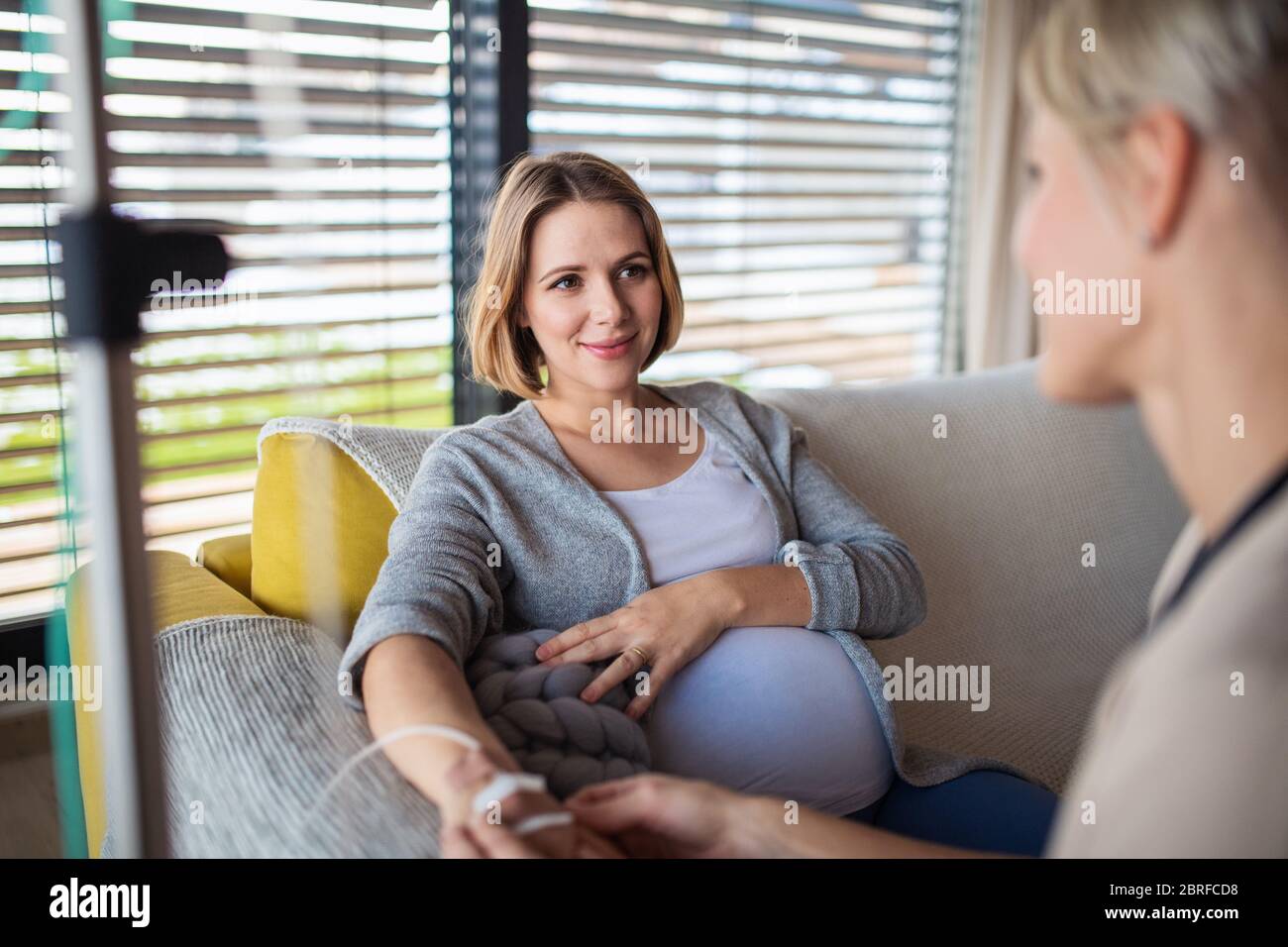 Healthcare worker with IV drip examining pregnant woman indoors at home. Stock Photo