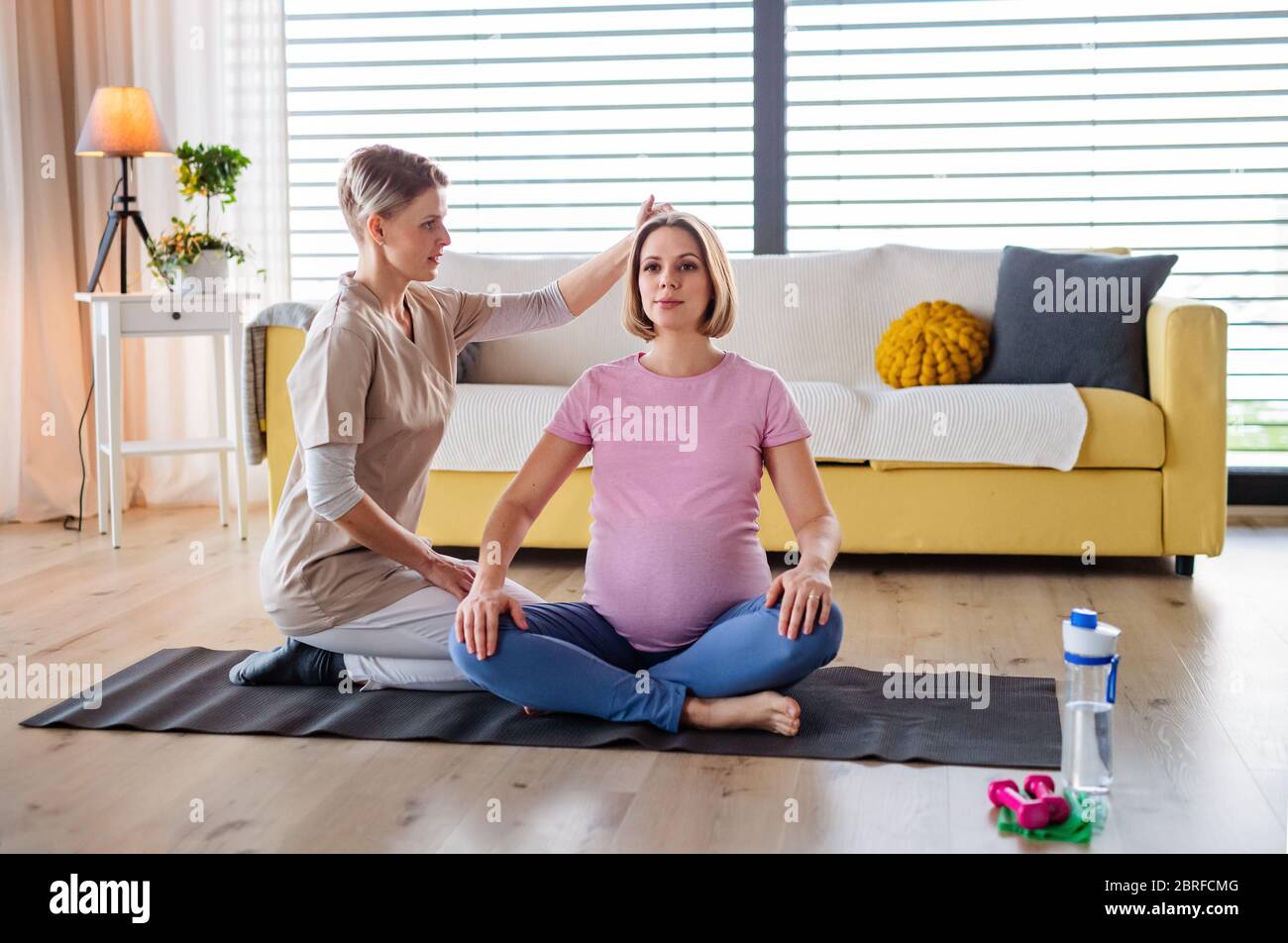 Pregnant woman doing yoga exercise with instructor at home. Stock Photo