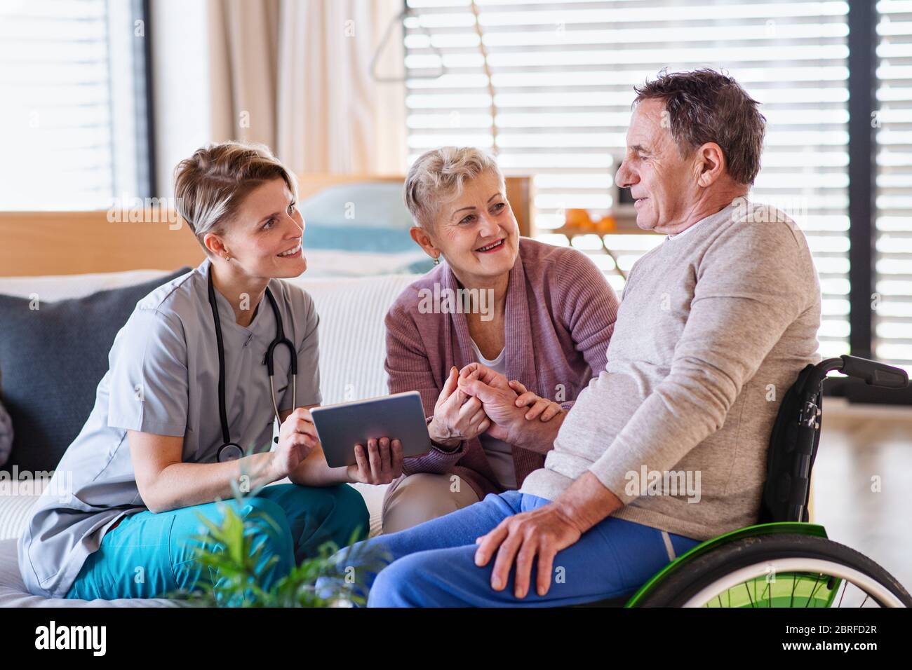 A healthcare worker visiting senior patient in wheelchair at home Stock