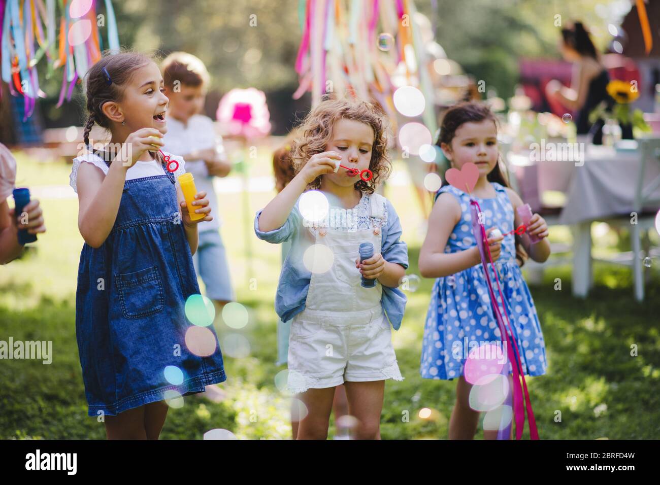 Small children outdoors in garden in summer, playing with bubbles. Stock Photo