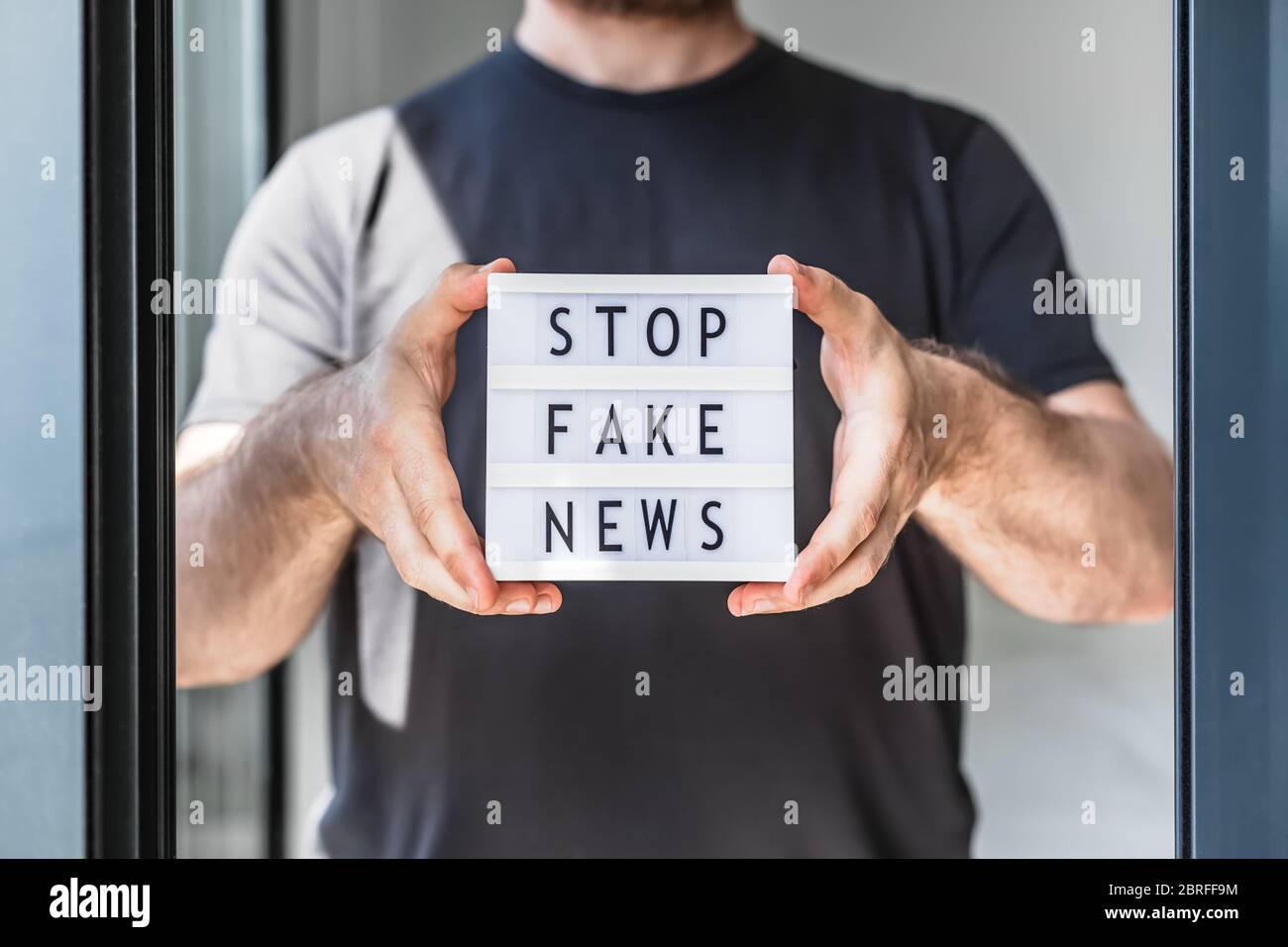 Fake news infodemics during Covid-19 pandemic concept. Man hands holding lightbox with text Stop fake news on foreground. People want to know the trut Stock Photo