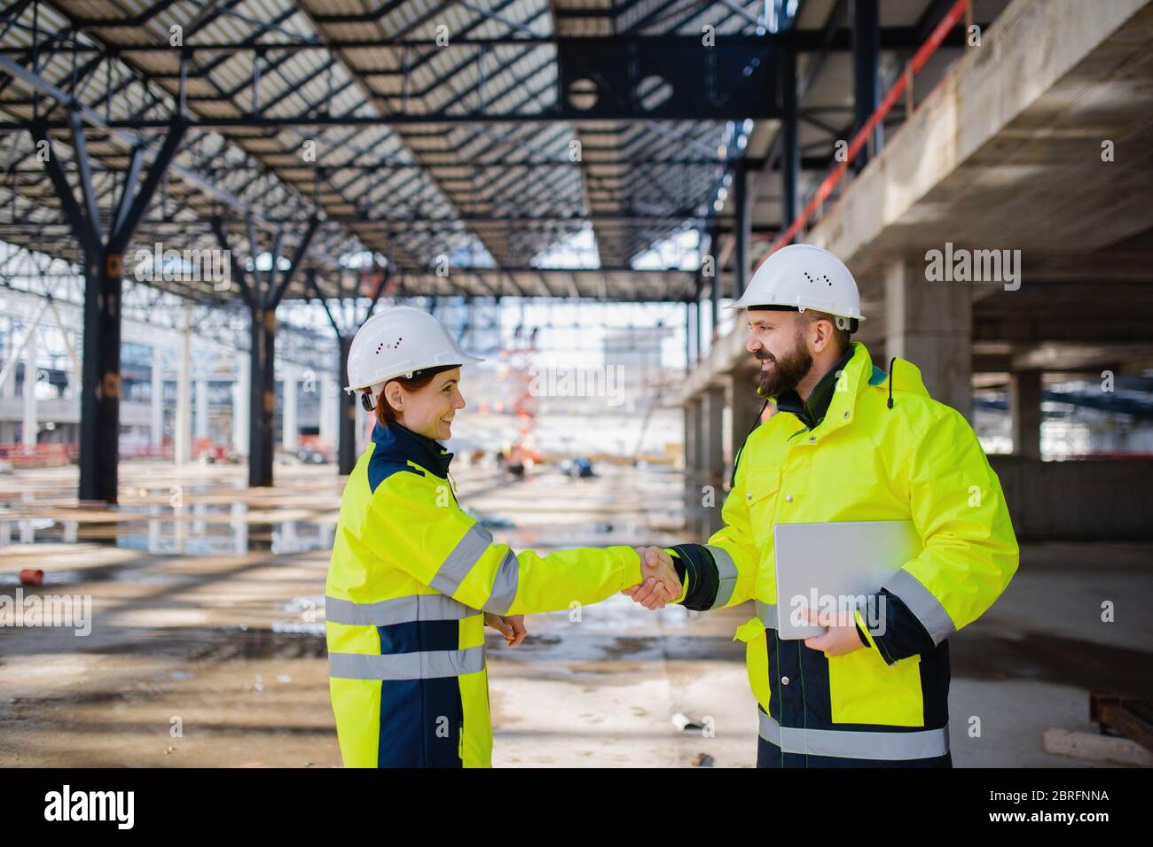 Engineers with tablet standing on construction site, shaking hands. Stock Photo