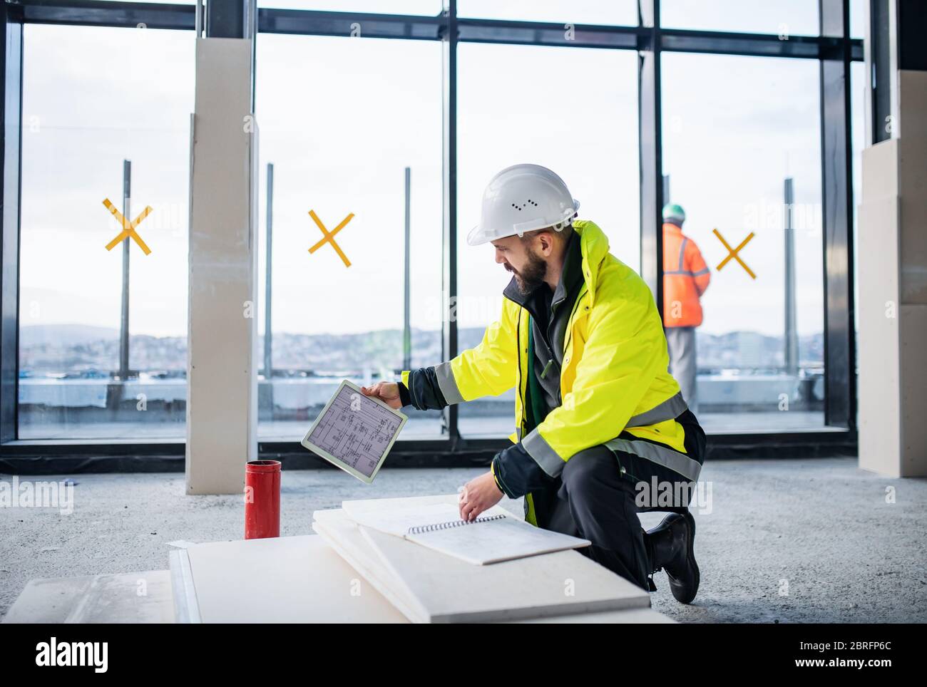 Man engineer with tablet on construction site, looking at blueprints. Stock Photo
