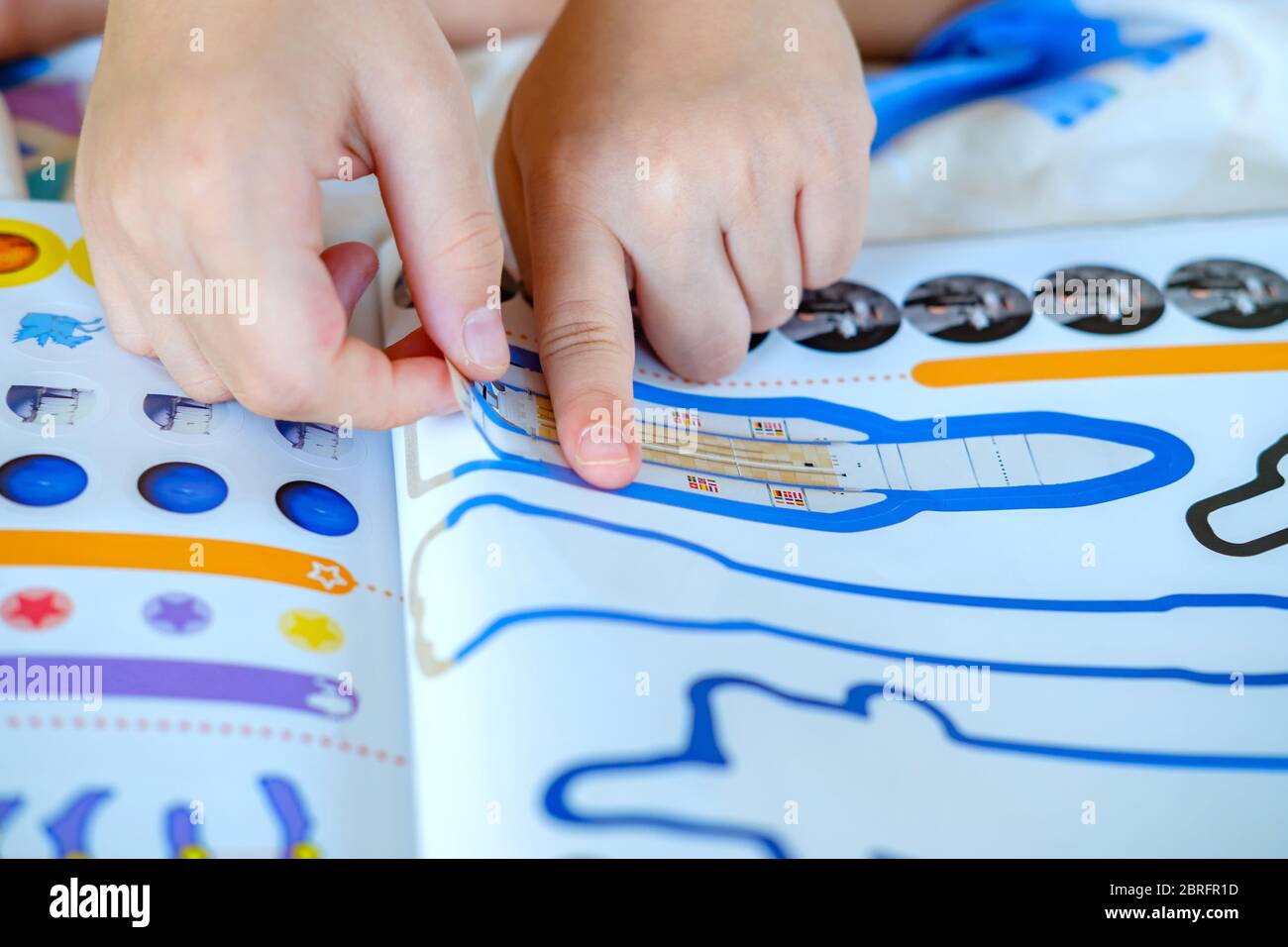 Child’s hand, Kid’s hand is sticking rocket sticker on space education activity book. Space education activity for school student. Stock Photo