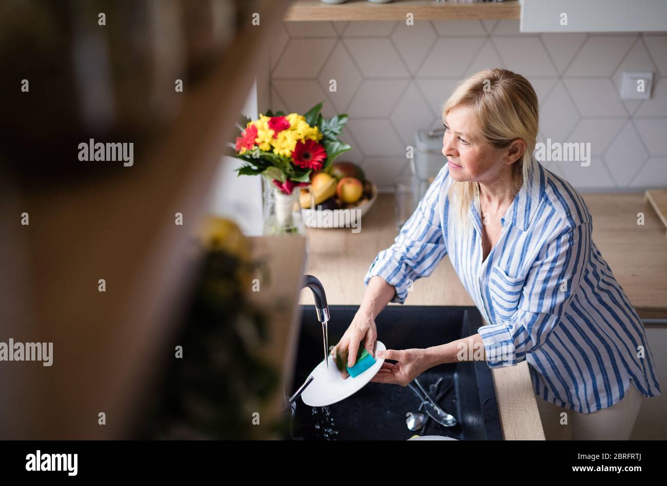 Portrait of senior woman washing dishes indoors at home. Stock Photo