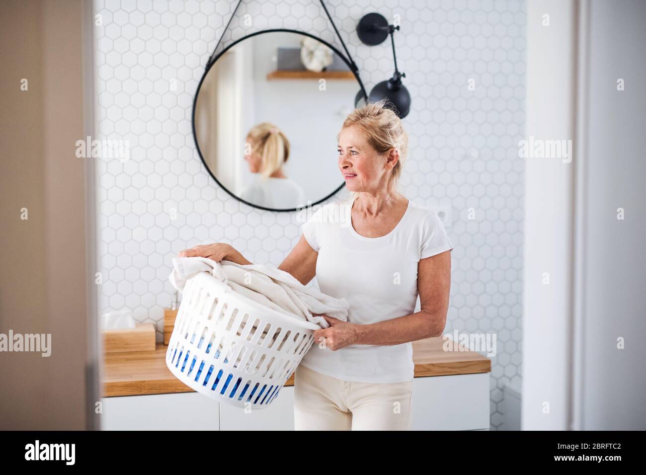 Portrait of senior woman with laundry basket indoors at home. Stock Photo