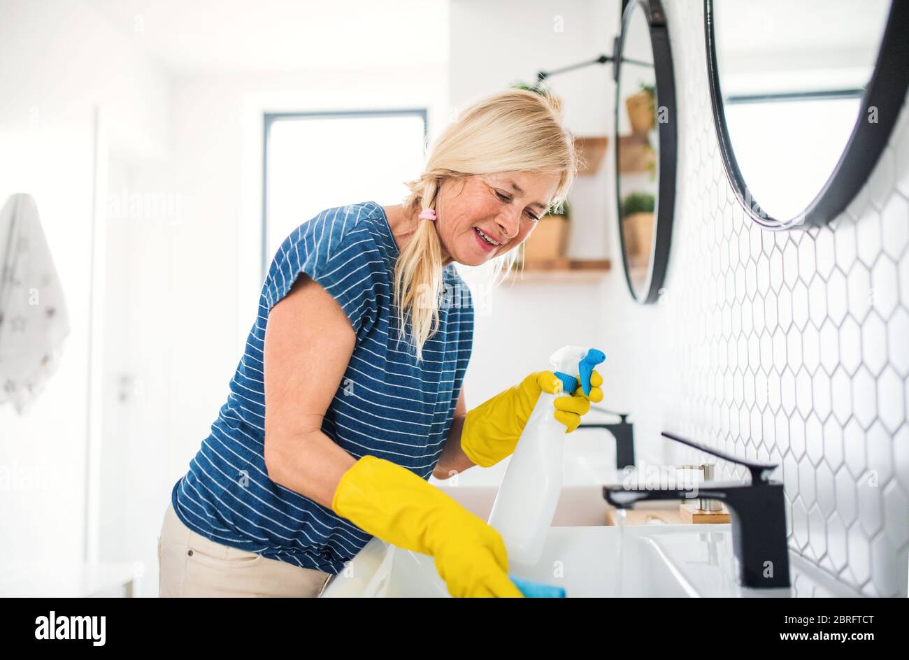 Senior woman with gloves cleaning bathroom indoors at home. Stock Photo