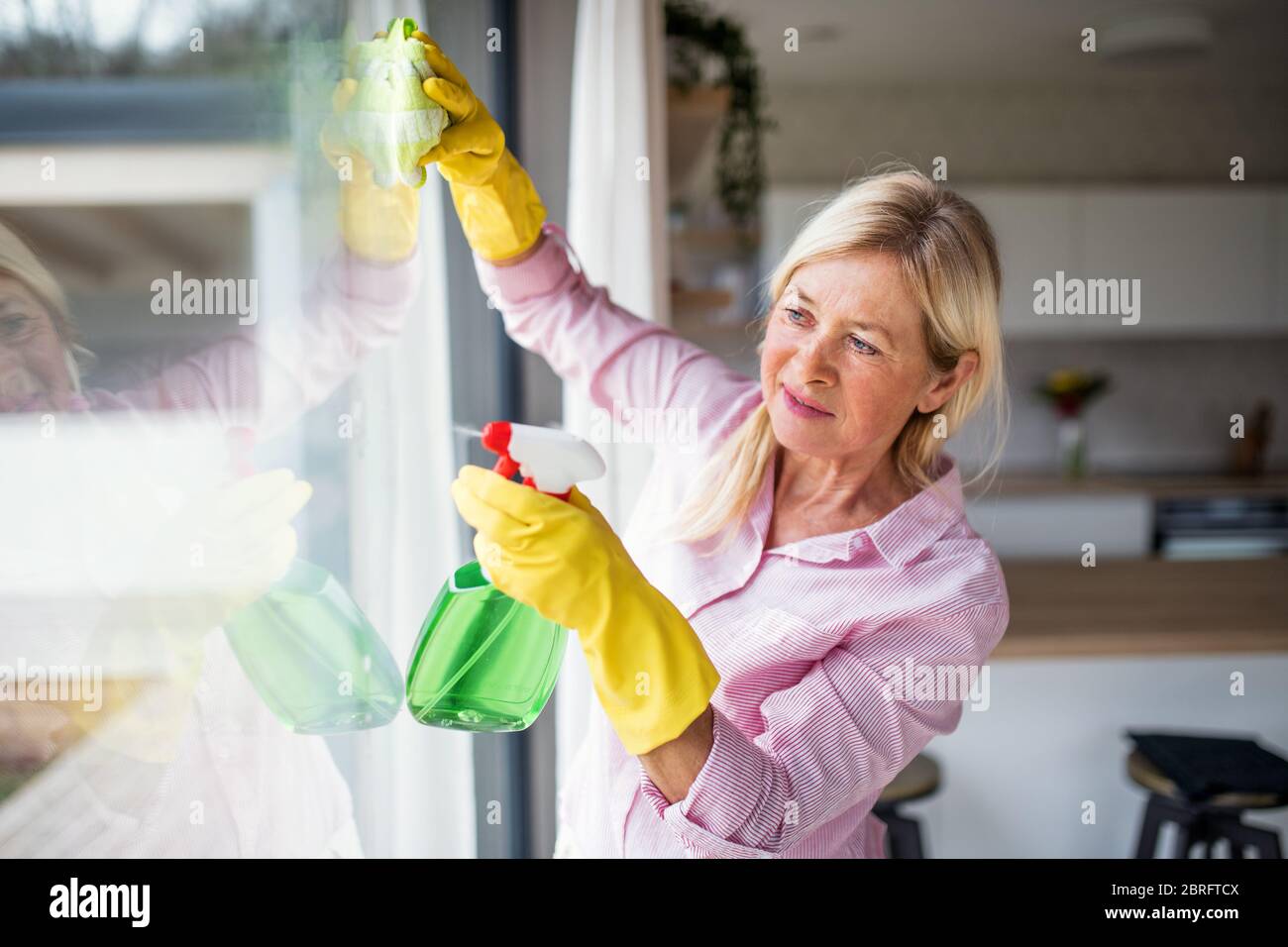 Portrait of senior woman cleaning windows indoors at home. Stock Photo