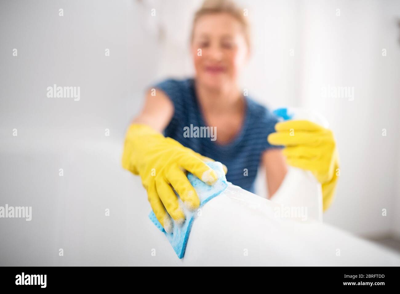 Senior woman with gloves cleaning bathroom indoors at home. Stock Photo