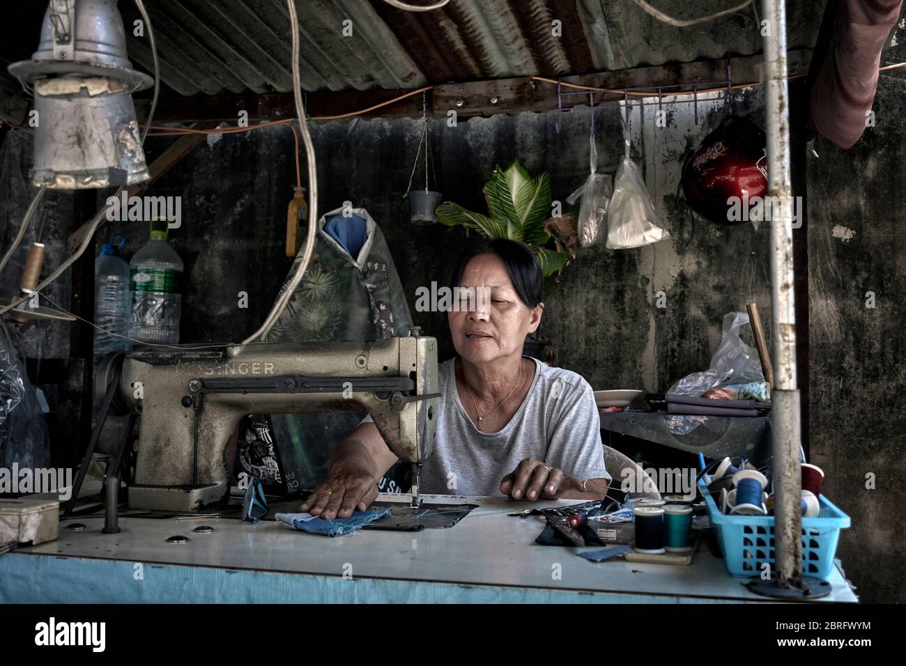 Woman working. Thailand Seamstress working at her back street stall using a vintage sewing machine. Southeast Asia Stock Photo