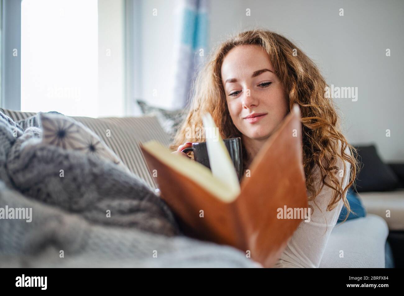 Young woman relaxing indoors at home with book. Stock Photo