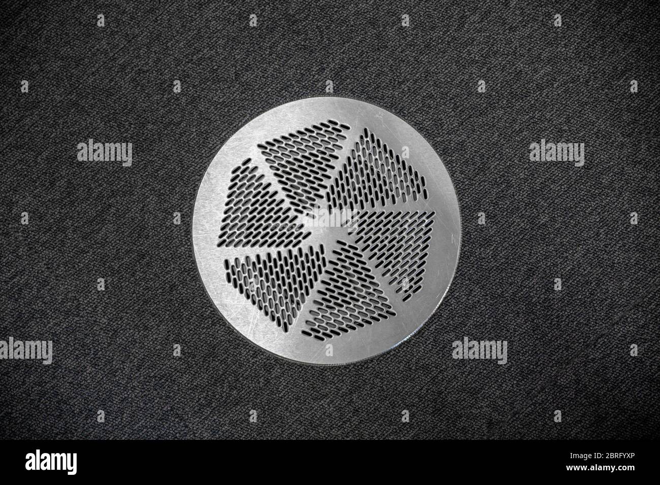 Close Up of Circular Metal Air Vent in Home Surrounded by Dark Grey Carpet Floor in a Office Building. Stock Photo