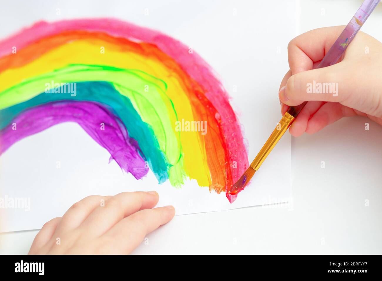 Close up of hands of child drawing rainbow by watercolors on white ...
