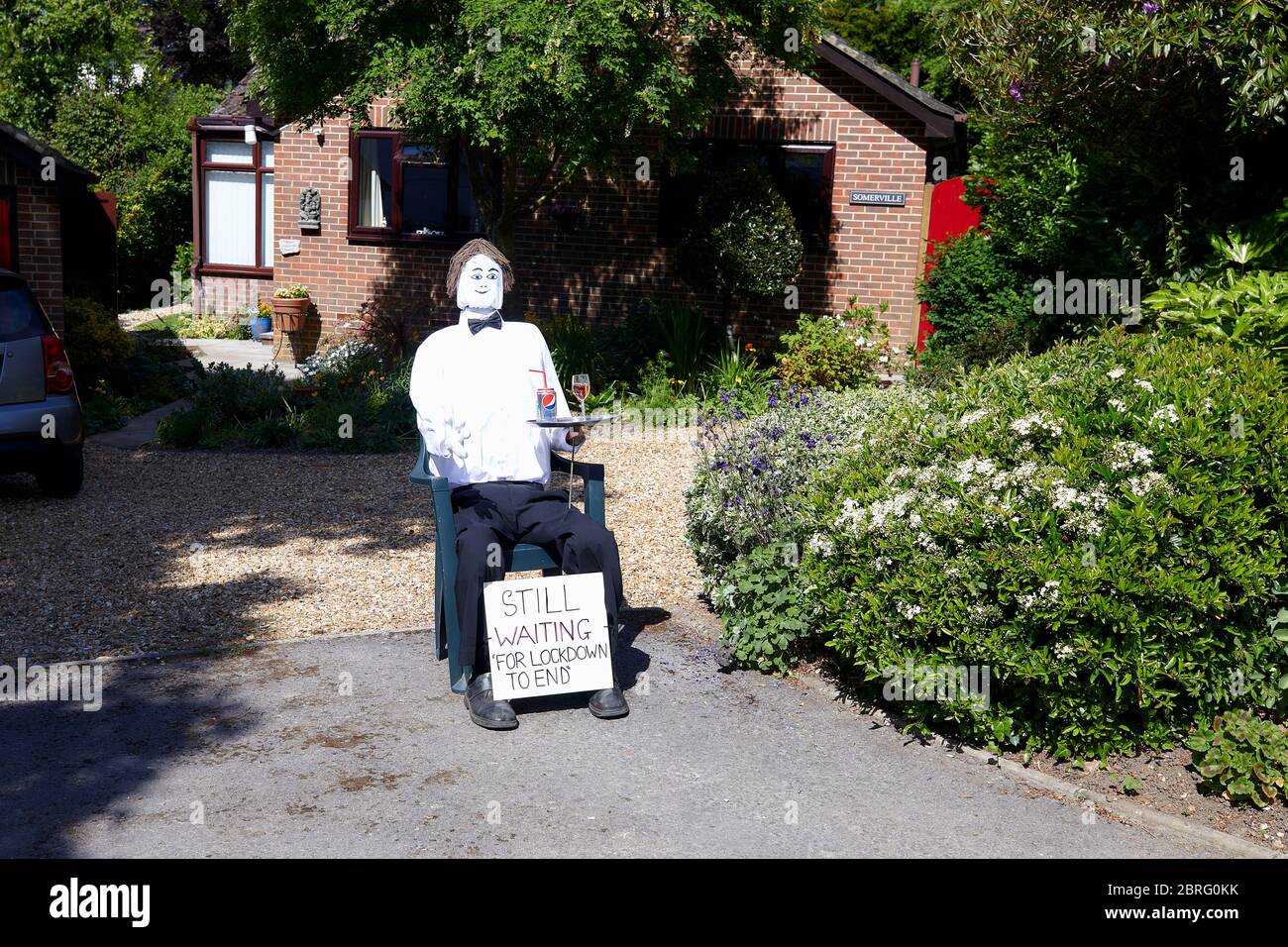 Sandleheath, UK. - May 20, 2020: A waiiter scarecrow outside a house. The Hampshire village of Sandleheath holds an annual scarecrow competition. Many entries this year adopt a coronavirus theme. Stock Photo