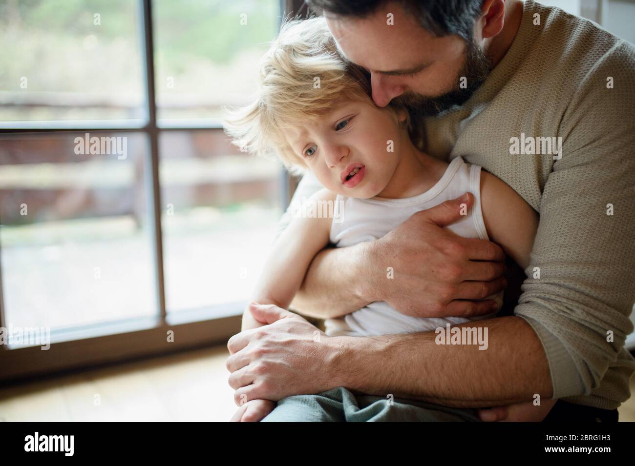 Father with small sick unhappy son indoors at home, comforting him. Stock Photo