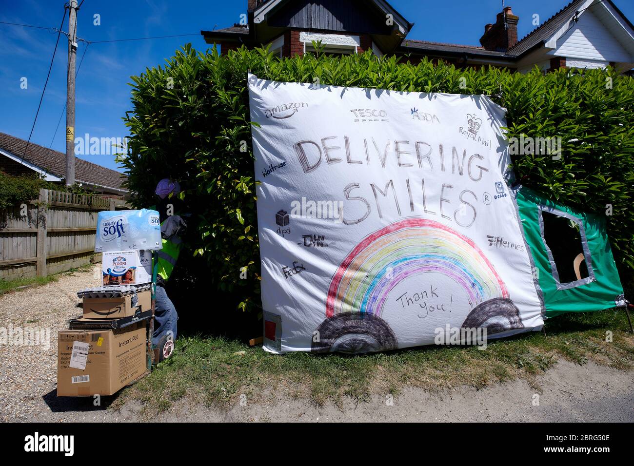 Sandleheath, UK. - May 20, 2020: A delivery worker themed scarecrow display outside a house. The Hampshire village of Sandleheath holds an annual charity scarecrow competition. Many entries this year adopt a coronavirus theme. Stock Photo