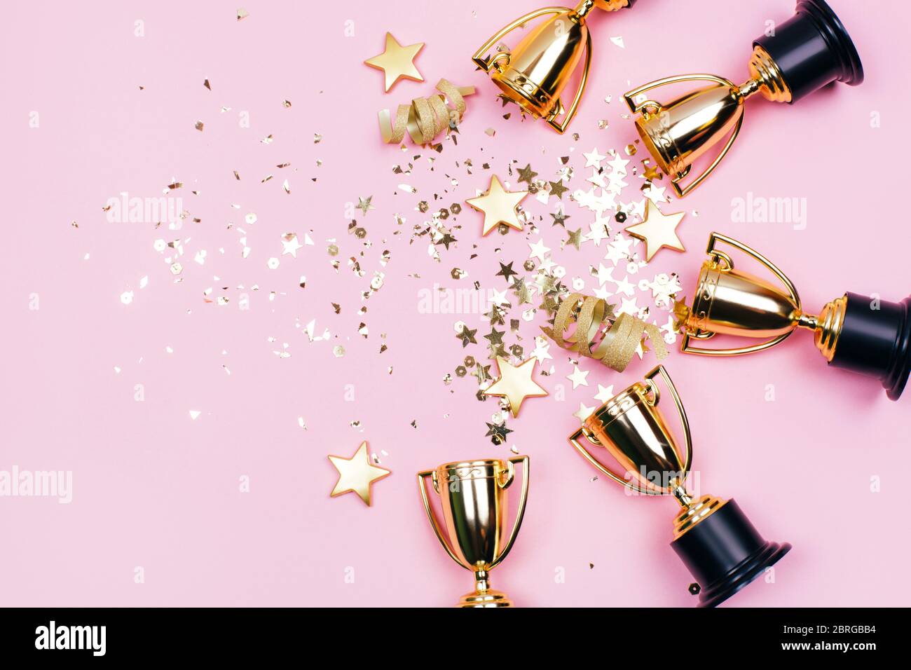 Golden winner cups with sparkles on a pink background with copy space. Festive concept. Flat lay style. Stock Photo