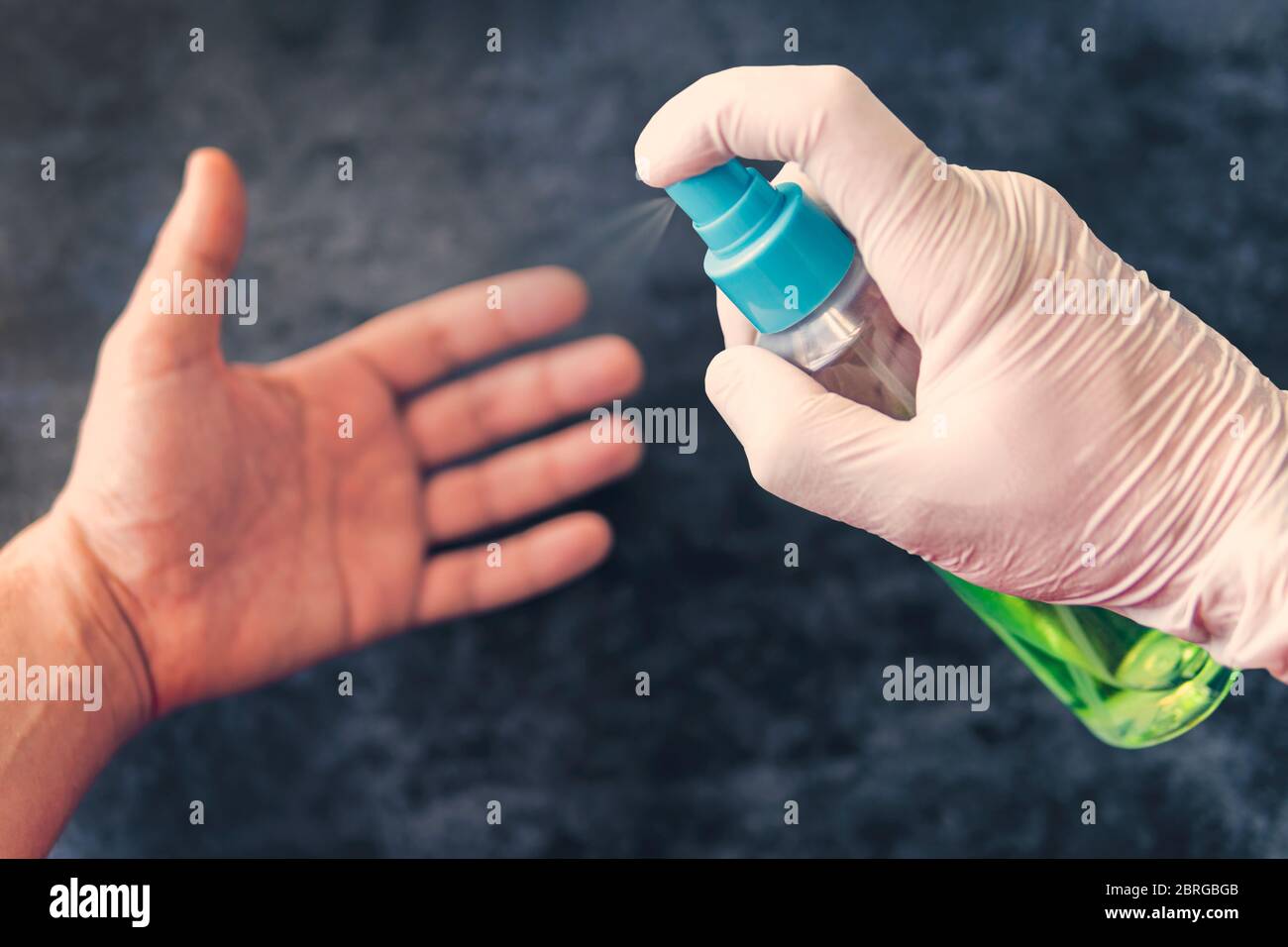 Cleaning of hands from bacteria and microbes with alcohol spray, prevention of coronavirus and other diseases. gloved hand sprays aerosol on a clean Stock Photo