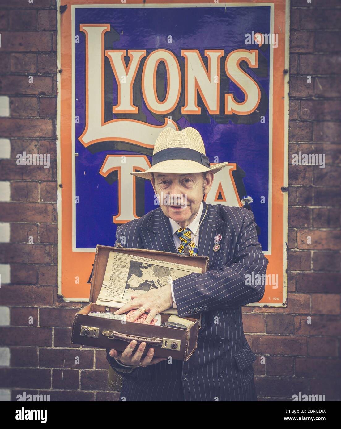 Close up 1940s spiv & vintage case of black market WW2 goods, 1940s WWII wartime summer event. Isolated ww2 spiv by railway station vintage Tea sign. Stock Photo