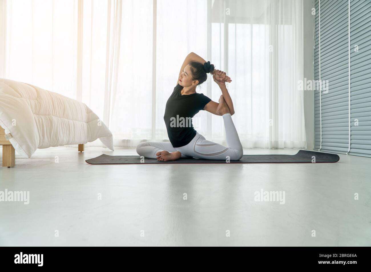 Middle aged women doing yoga in bedroom at the morning, adho mukha svanasana pose. Concept of exercise and relaxation in the morning. Stock Photo