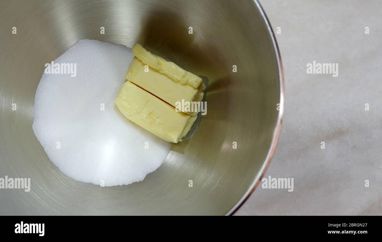 Chunks of butter and white sugar, in metal mixing bowl, placed on a marble surface. Stock Photo