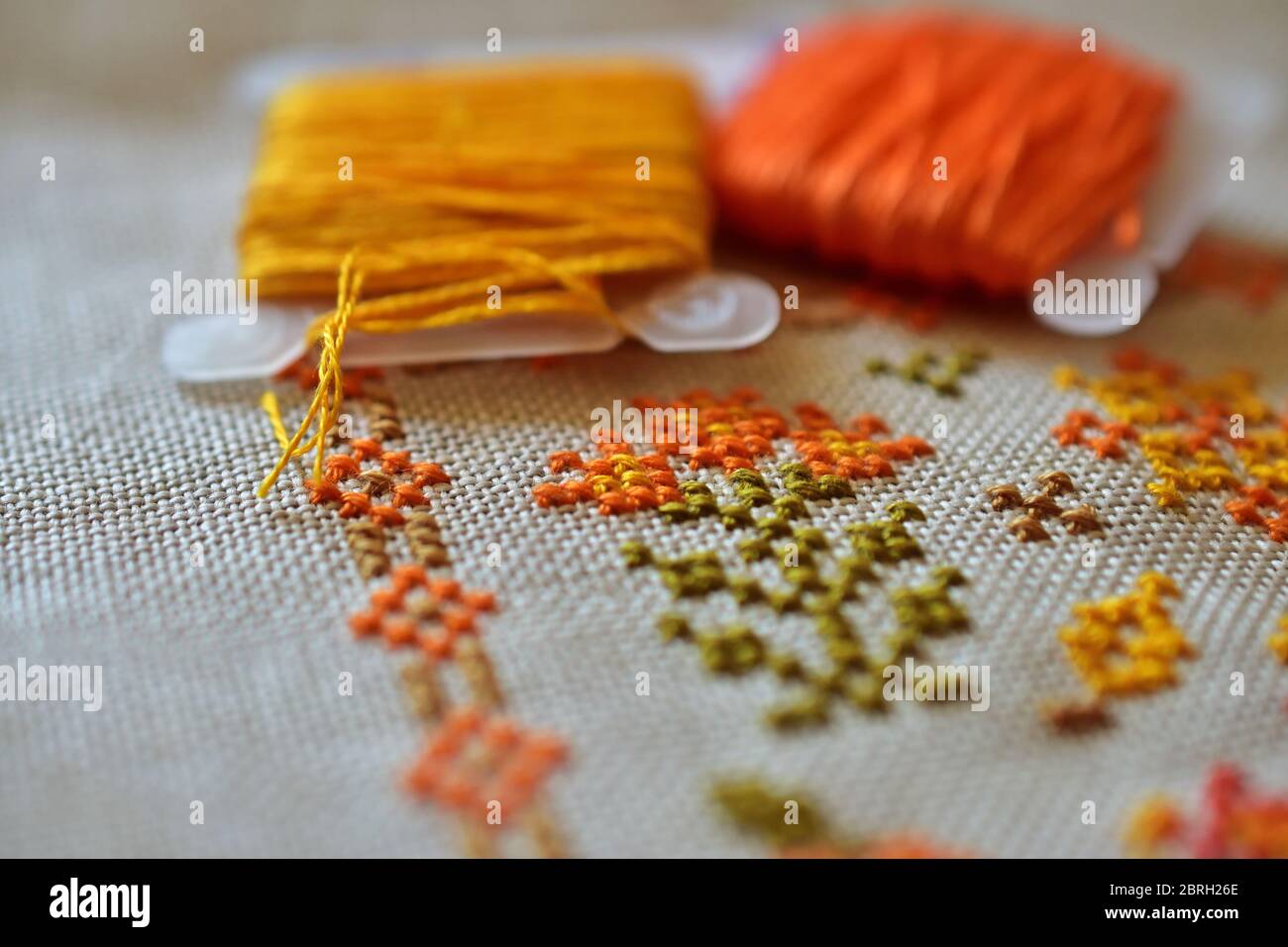 Cross stitch, linen and yellow and orange yarn, up close Stock Photo