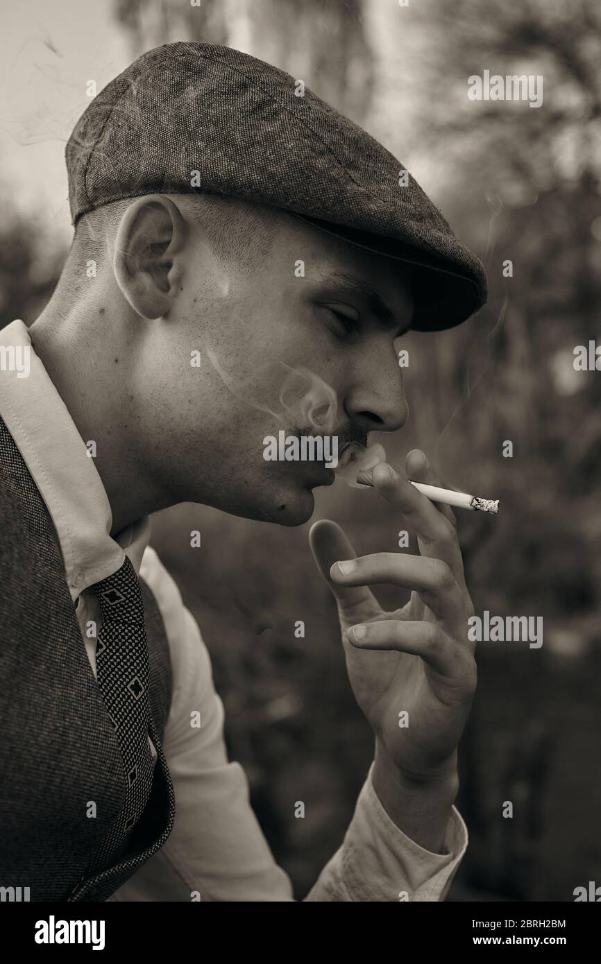 Retro 1920s portrait of an English gangster with a flat cap. Smokes a