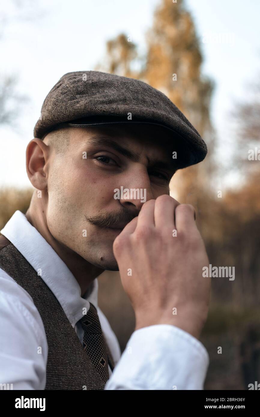 Retro 1920s portrait of an English gangster with a flat cap. Smokes a