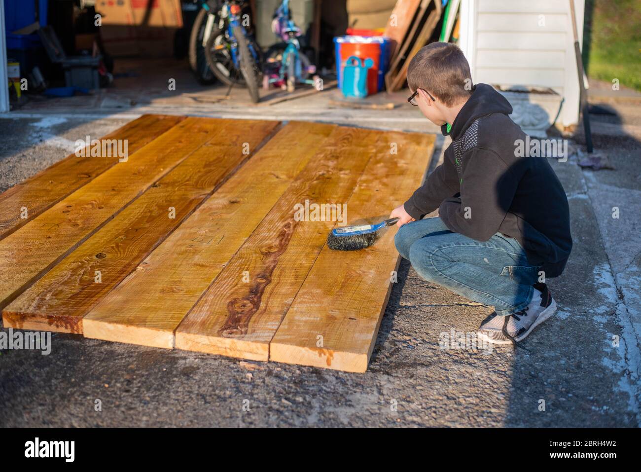 A boy paints boards with linseed oil to treat them for use in a raised
