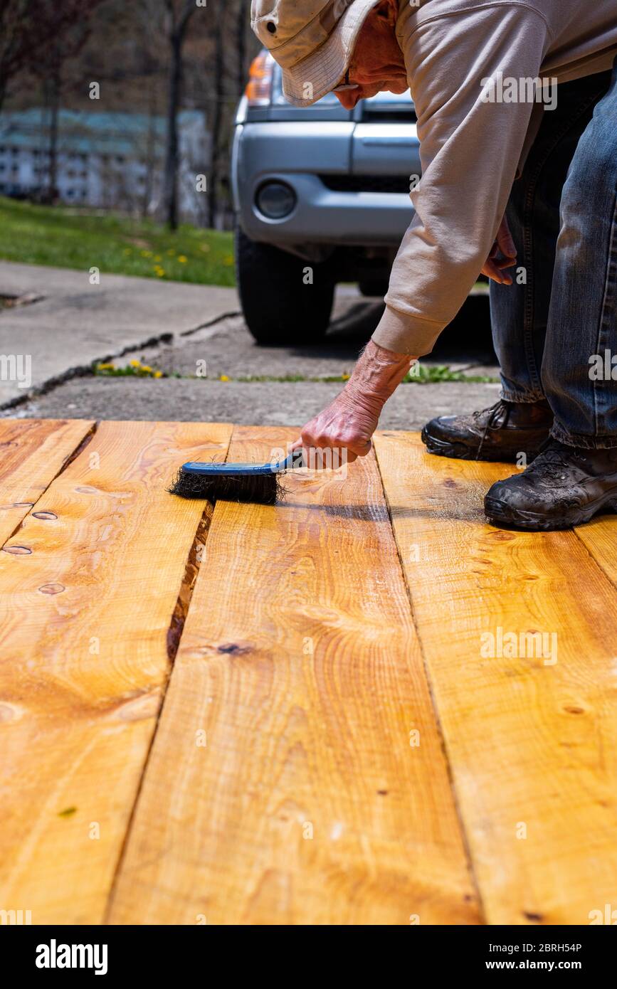 A man paints boards with linseed oil to treat them for use in a raised garden bed Stock Photo