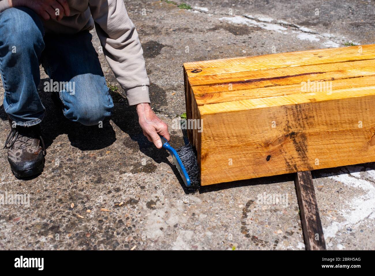 A boy sprays boards with linseed oil to treat them for use in a raised