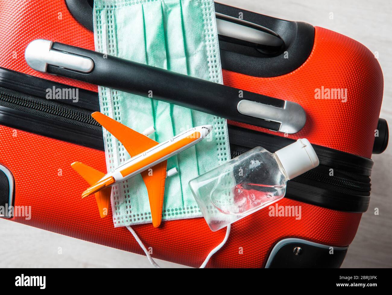 Flat lay view of medical face mask with airplane figurine on traveling baggage suitcase with small portable hand sanitizer bottle. Stock Photo