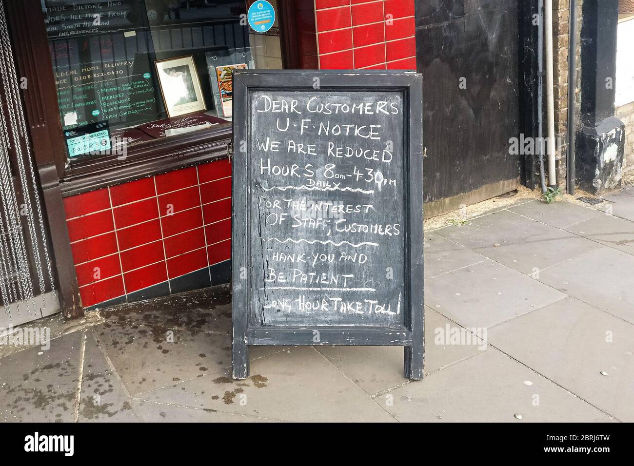 London, United Kingdom - April 27, 2020: Chalk hand written notice on blackboard in front of John Charles Butchers shop about reduced opening hours du Stock Photo