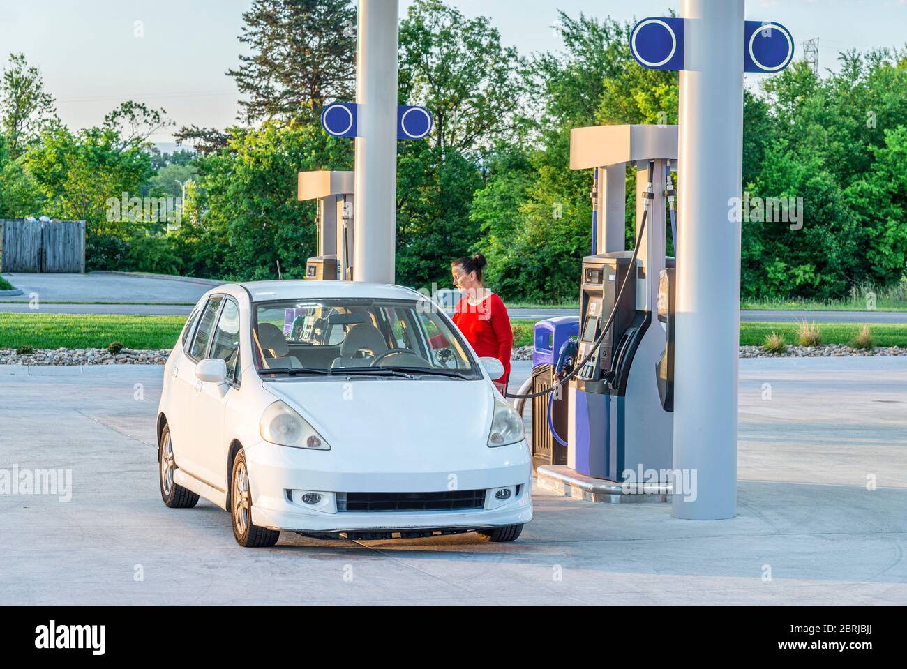 Horizontal shot of a woman making an early morning gasoline purchase for her white car. Stock Photo
