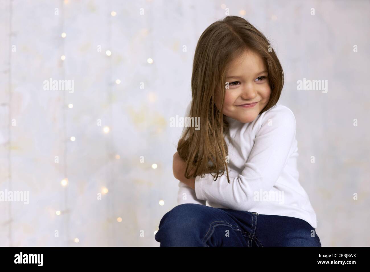 Portrait of a smiling little girl on a light background decorated with garlands. Stock Photo