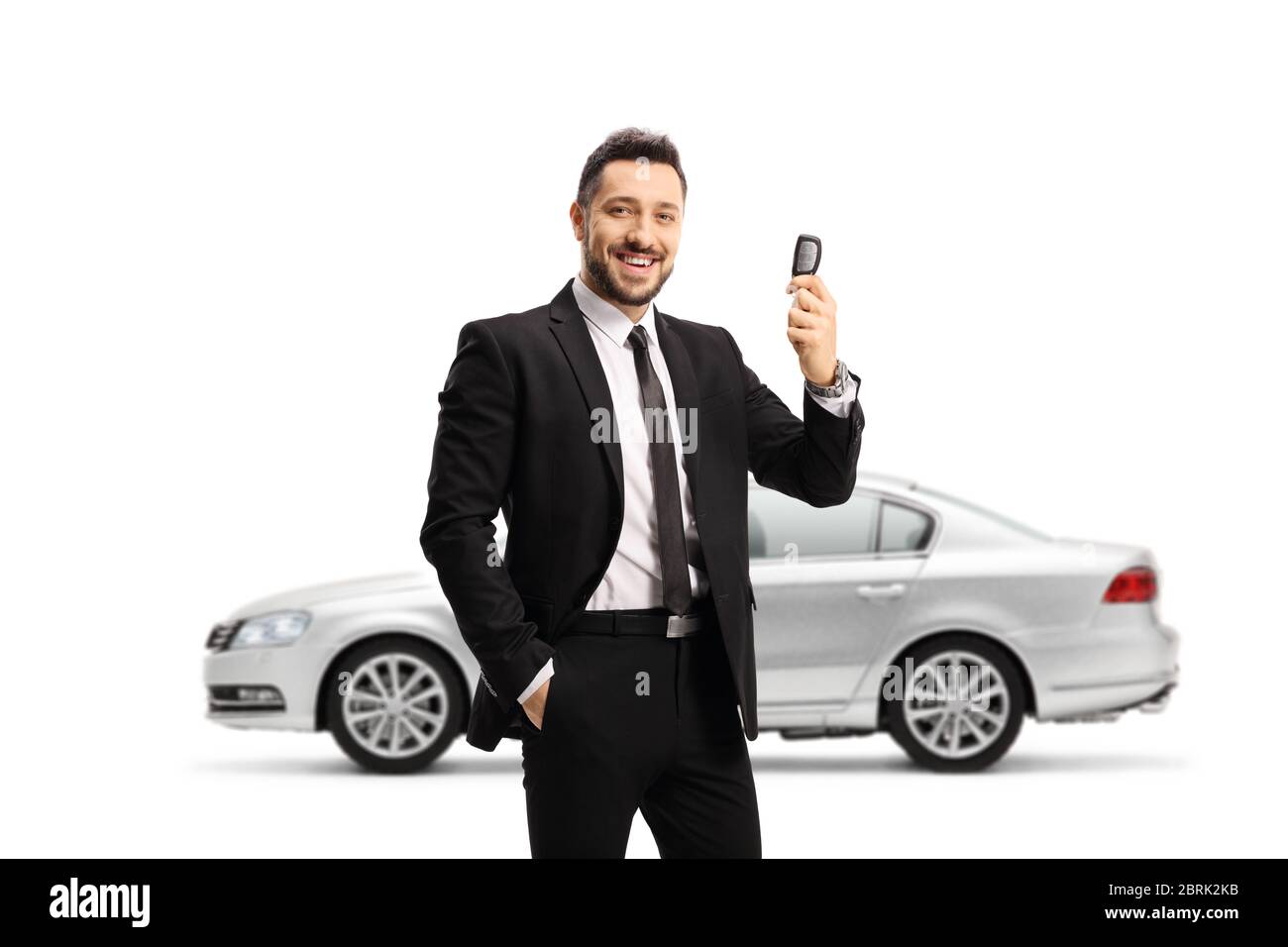Man in a suit showing car keys and and standing in front of a silver car isolated on white background Stock Photo