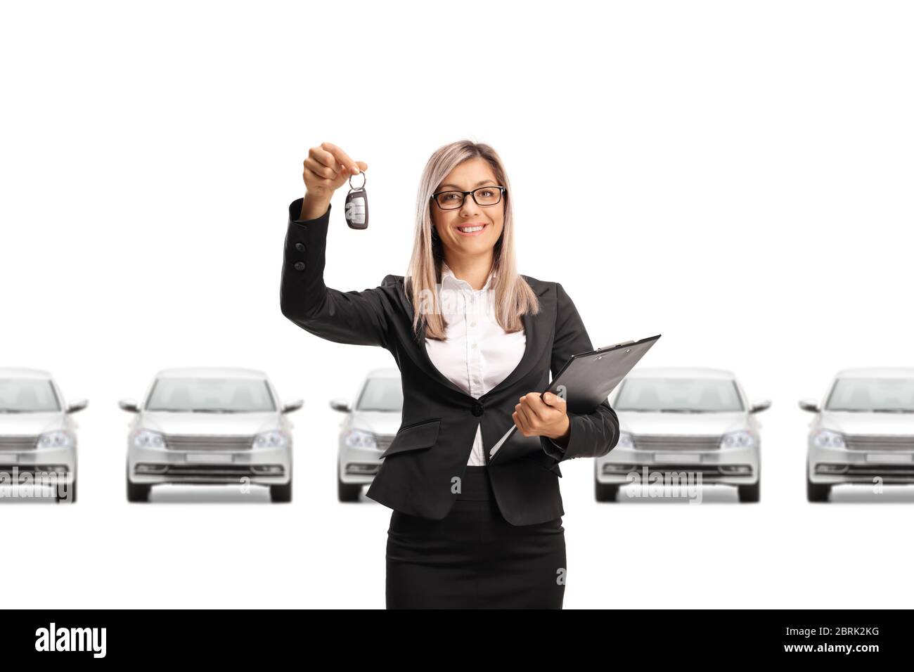 Professional sales woman showing car keys and row of cars behind isolated on white background Stock Photo