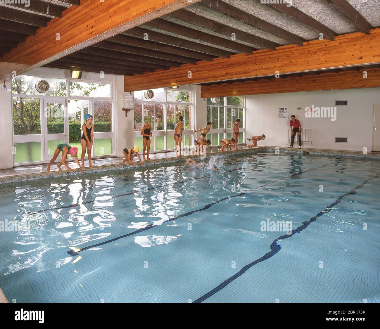 School children diving into indoor swimming pool, West Sussex, England