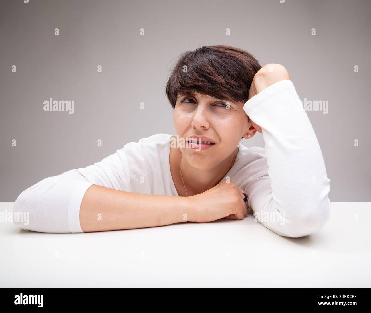 Puzzled or anxious woman deep in thought resting her head on her hand and elbow looking up with a frown of concentration in a close up portrait agains Stock Photo