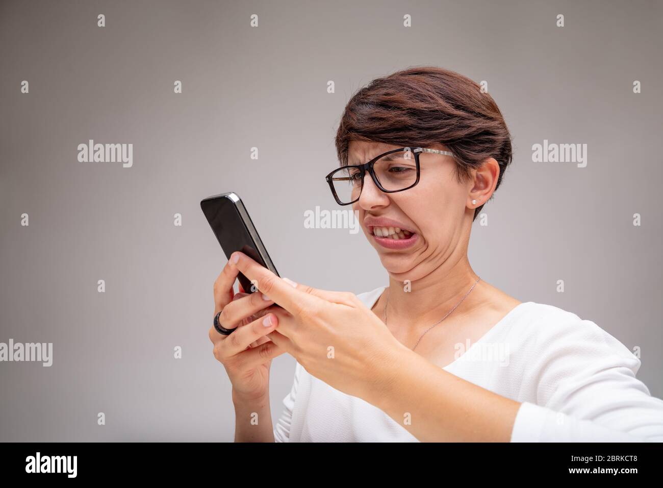 Woman reacting in revulsion to her mobile phone grimacing and pulling a face showing her repugnance in a close up portrait Stock Photo