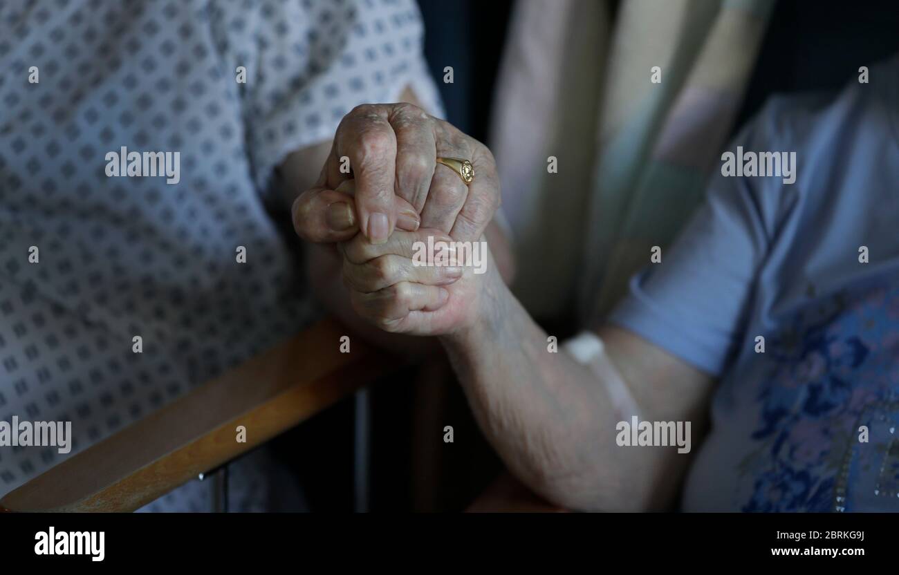 Coronavirus patients George Gilbert, 85 and his wife Domneva Gilbert 84, hold hands during a short visit, they are being treated in different areas, and both are part of the TACTIC-R trial, at Addenbrooke's hospital in Cambridge. Stock Photo